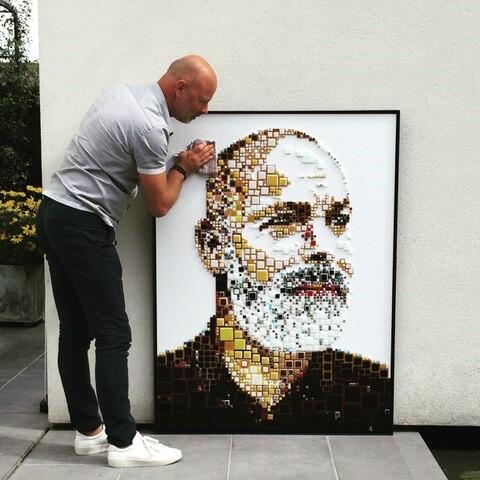Man leunt tegen groot portret met mozaïek van een bebaarde man.
