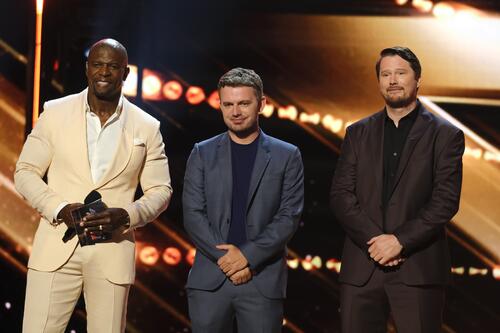 Mannen in pakken staan op een podium met gouden achtergrond.