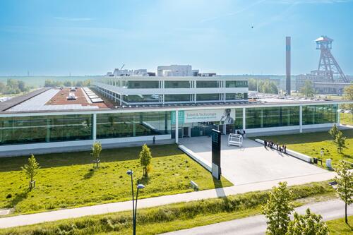 Moderne, glazen kantoorgebouw met parkje en heldere lucht.