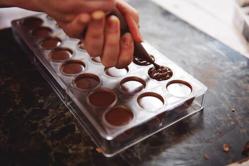Chocolade wordt in een mal gegoten, handen zichtbaar.