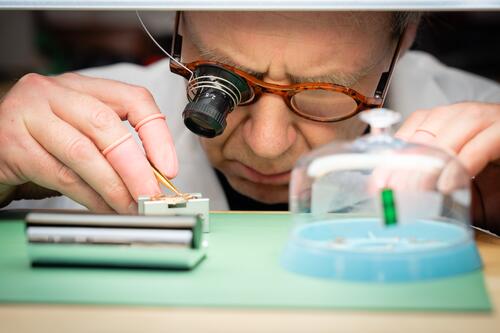 Persoon met loep onderzoekt klein object op groene mat in laboratorium.