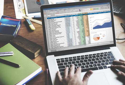 Open laptop met spreadsheet en grafieken, handen op toetsenbord.