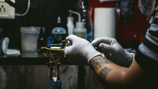 Tattoo-artiest bereidt inktmachine voor in donkere studio.