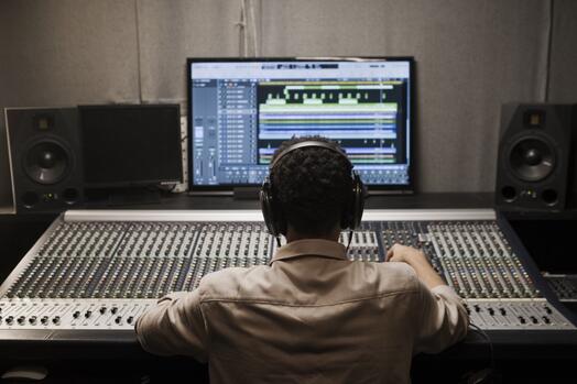 Man met hoofdtelefoon werkt aan mengpaneel in opnamestudio.