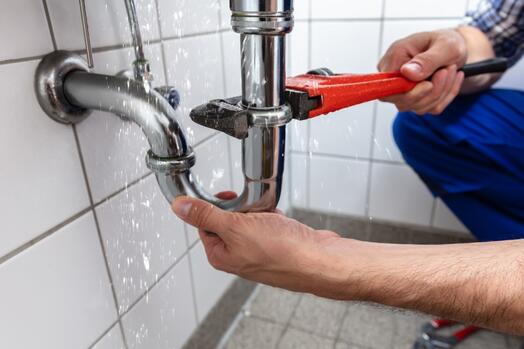 Handen repareren leiding onder wastafel met een moersleutel.