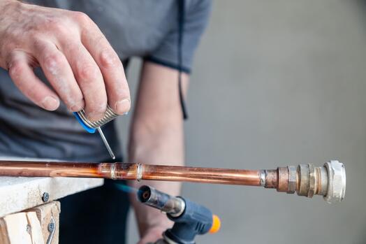 Persoon soldeert koperen pijp met een brander.