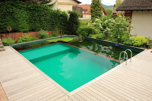 Natuurlijk zwembad in tuin met houten terras en groene planten.