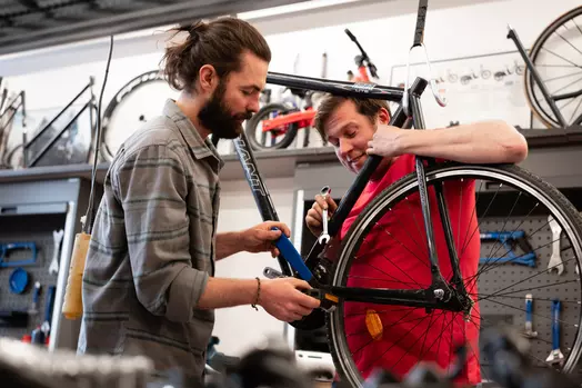 Twee mannen repareren een fiets in een werkplaats.