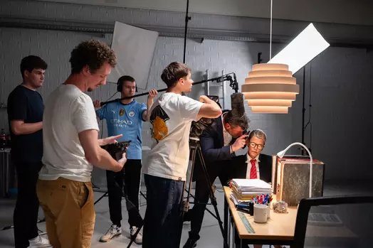 Filmploeg zet een persoon klaar voor opname in studio met camera en belichting.