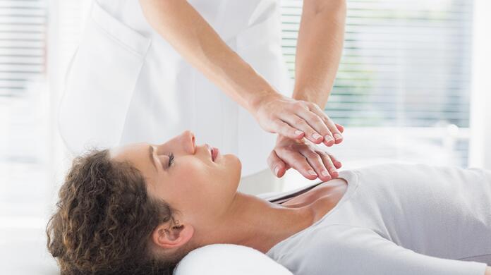 Vrouw ontvangt een Reiki-behandeling, ontspannen liggend met gesloten ogen.