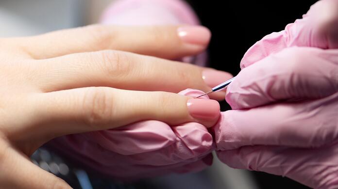 Nagels worden verzorgd door iemand met roze handschoenen.