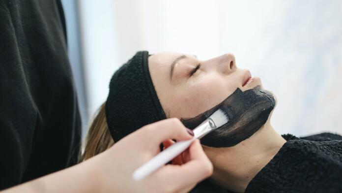 Vrouw krijgt gezichtsmasker aangebracht met kwast in salon.