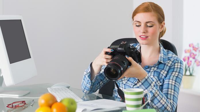 Vrouw bekijkt camera aan bureau met fruit en kopje koffie.