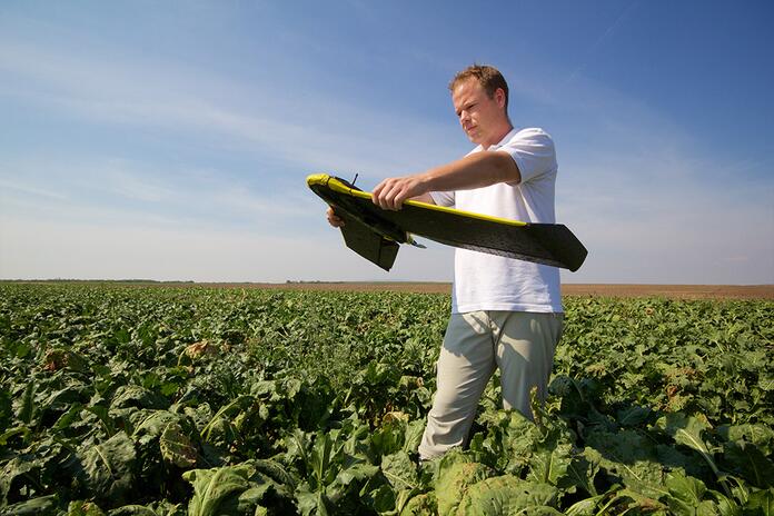 Man in gewasveld bestuurt drone onder blauwe hemel.