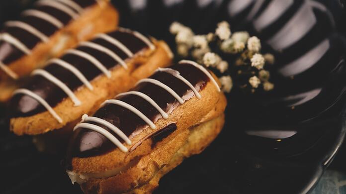 Chocolade-éclairs op een zwarte schaal met witte bloemetjes.