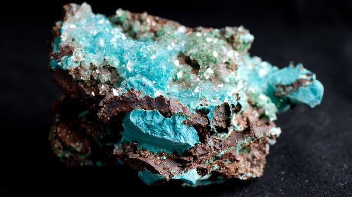Turquoise mineraal met ruwe kristallen op zwarte achtergrond.
