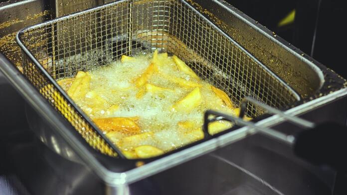 Frietjes worden gefrituurd in een mandje in heet vet.
