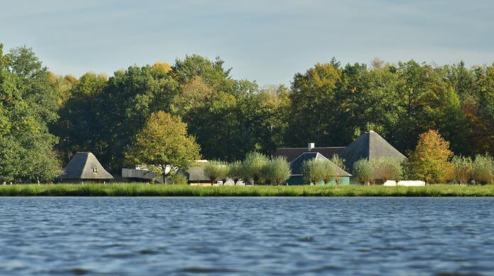 Landelijke huizen aan de oever van een meer, omgeven door bomen in de herfst.