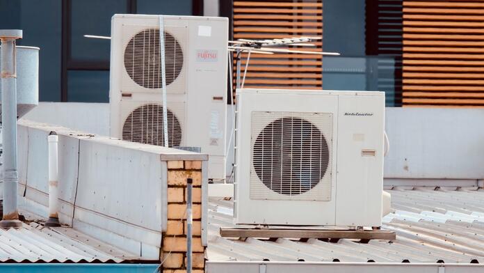 Twee airconditioners op een dak met houten lamellen op de achtergrond.