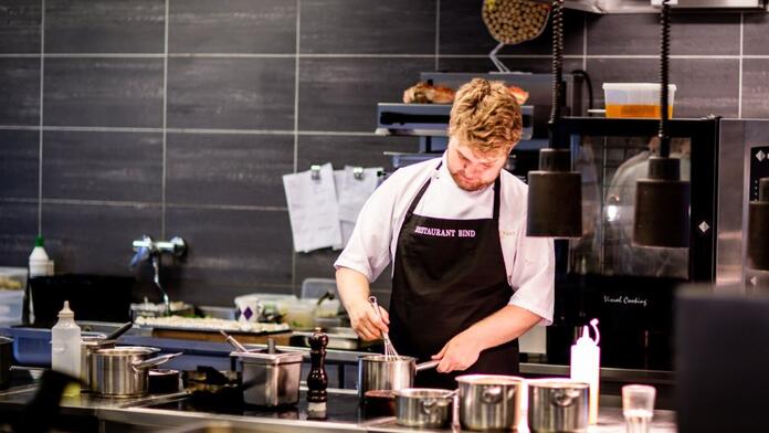 Chef in moderne keuken roert in een pan met geconcentreerde blik.