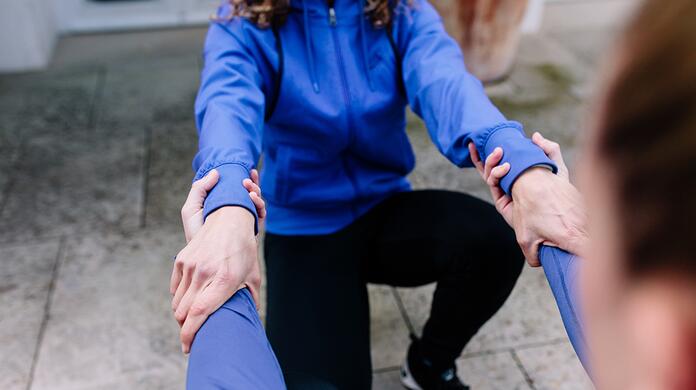 Twee mensen helpen elkaar omhoog buiten in sportkleding.