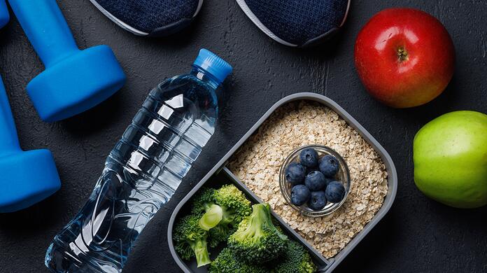 Blauwe halters, waterfles, gezonde lunchbox, rode en groene appel op tafel.
