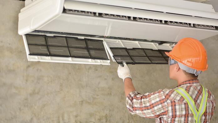 Man met oranje helm onderhoudt airconditioner.