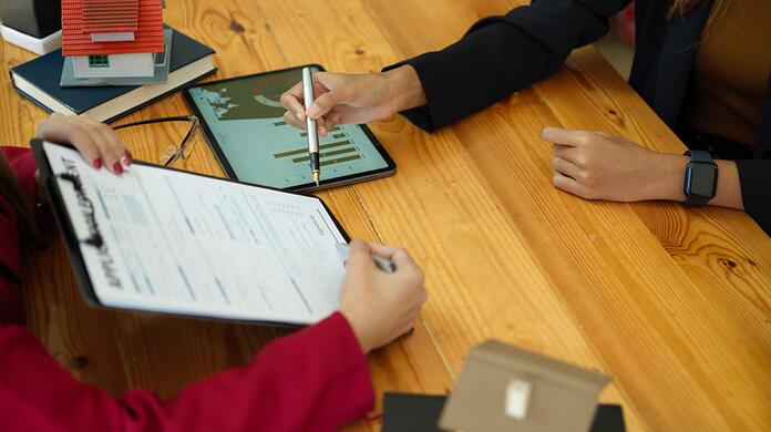Twee personen aan tafel met tablet en formulier, houten tafel.