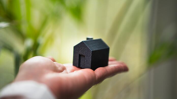 Zwarte miniatuurhuisje op een hand, groene achtergrond.