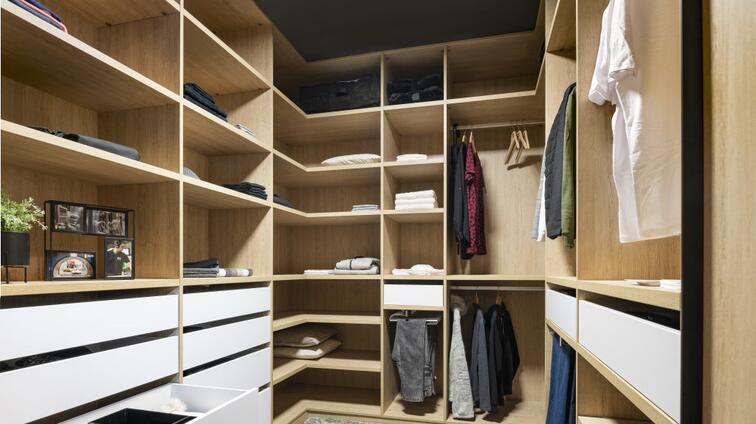 Luxe inloopkast met houten planken, lades en hangende kleding.
