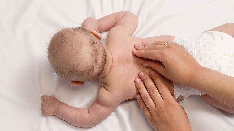 Baby krijgt massage op witte lakens.
