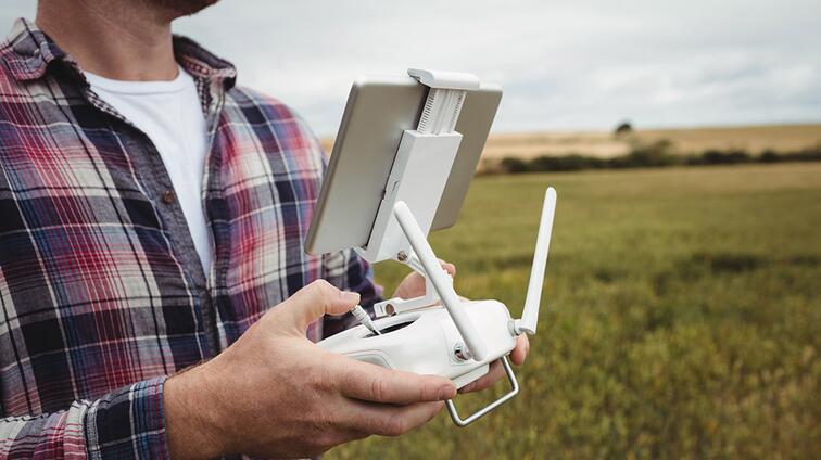 Man bestuurt drone buiten in een veld met tabletcontroller.