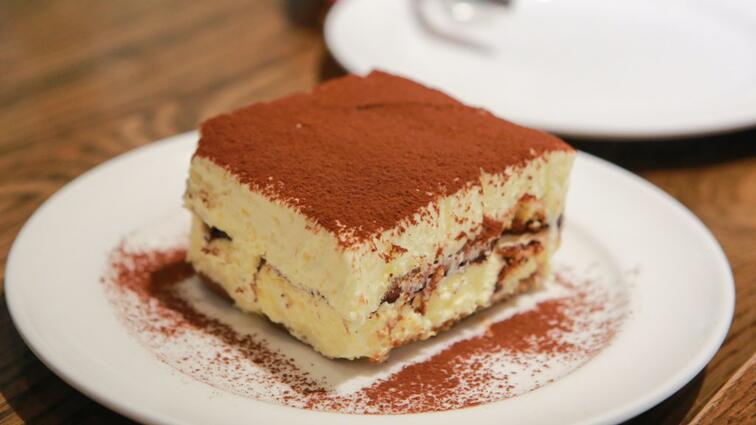 Tiramisu op een wit bord, bestrooid met cacao.