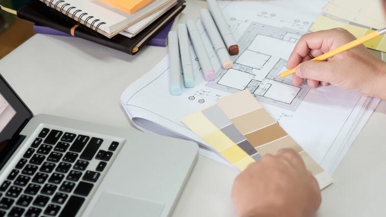 Ontwerper schetst op papier met kleurstalen en een laptop ernaast.