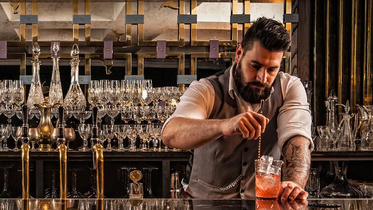 Barman mengt drankje met concentratie, glazen in achtergrond.