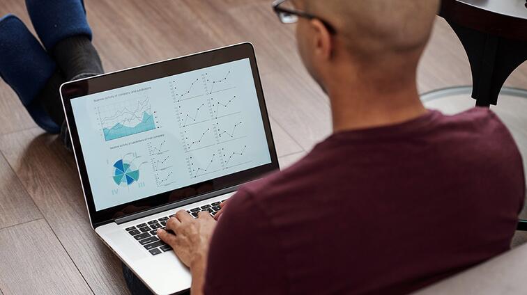 Man met bril werkt op laptop met grafieken op het scherm.