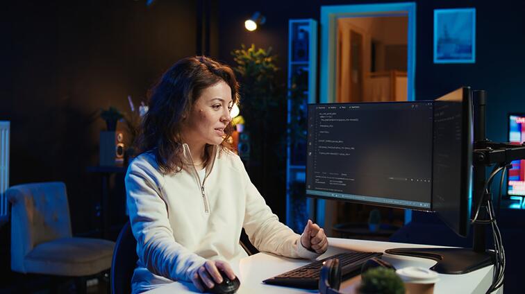 Vrouw programmeert op een computer in een moderne, donkere kantooromgeving.