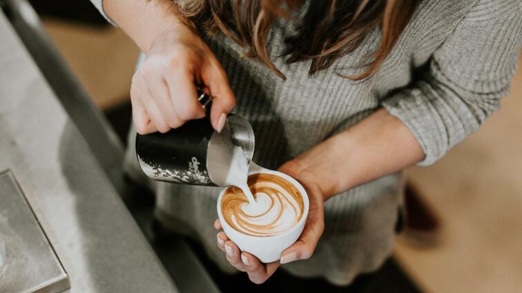 Persoon schenkt melk in koffie, creëert latte art.