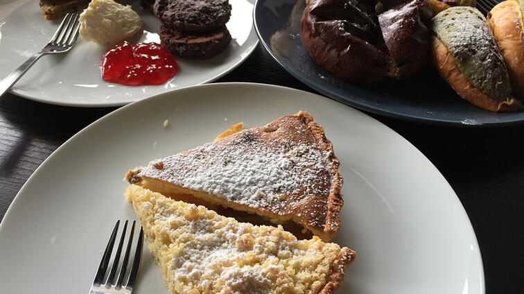 Twee punten taart met poedersuiker, broodjes en jam op borden.