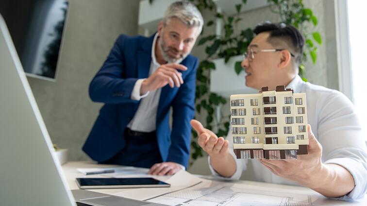 Twee mannen bespreken een architectonisch model aan een bureau.