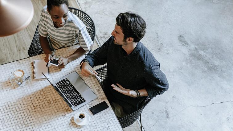 Twee mensen werken samen aan een tafel met laptop en notitieboekje.
