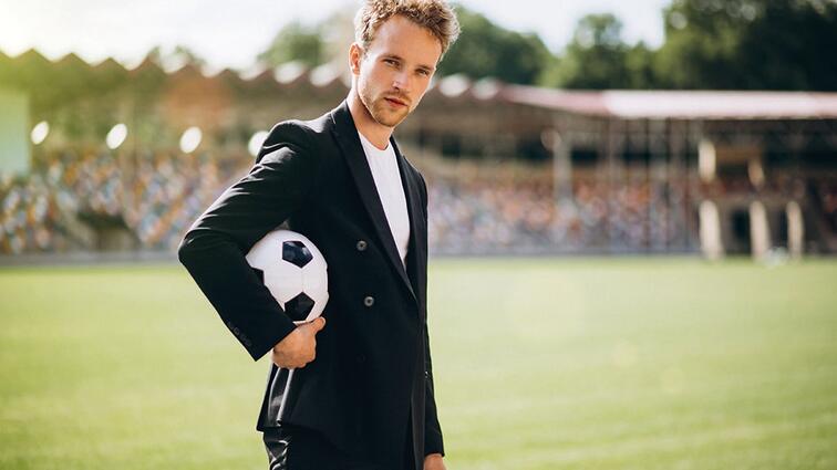 Man in pak houdt voetbal vast op sportveld, zonnige dag.