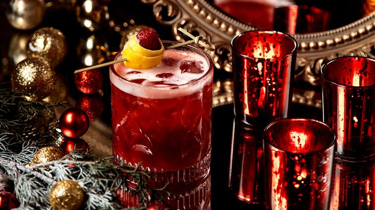 Rode cocktail met citroen en framboos, omringd door rode kaarsen en kerstversiering.