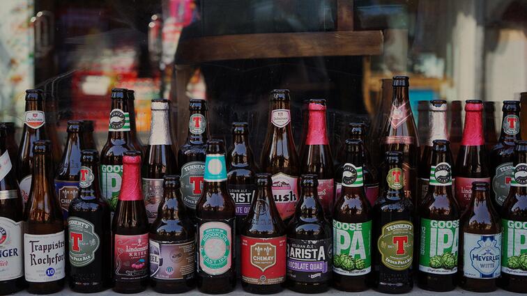 Verschillende bierflesjes in een rij voor een raam.