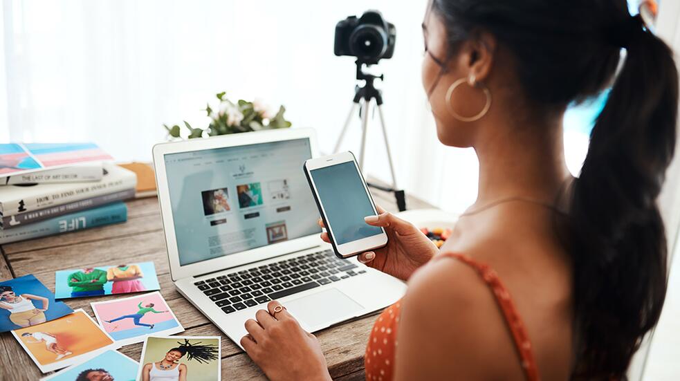 Vrouw werkt aan laptop met smartphone, omgeven door foto's.