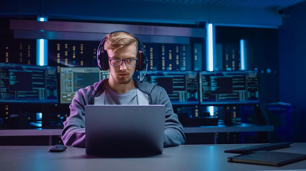 Persoon met koptelefoon werkt op laptop in serverruimte.