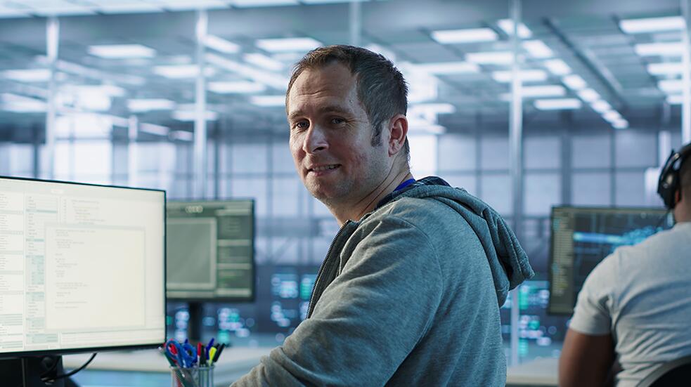 Man in grijze trui werkt aan computer in moderne kantoorruimte.