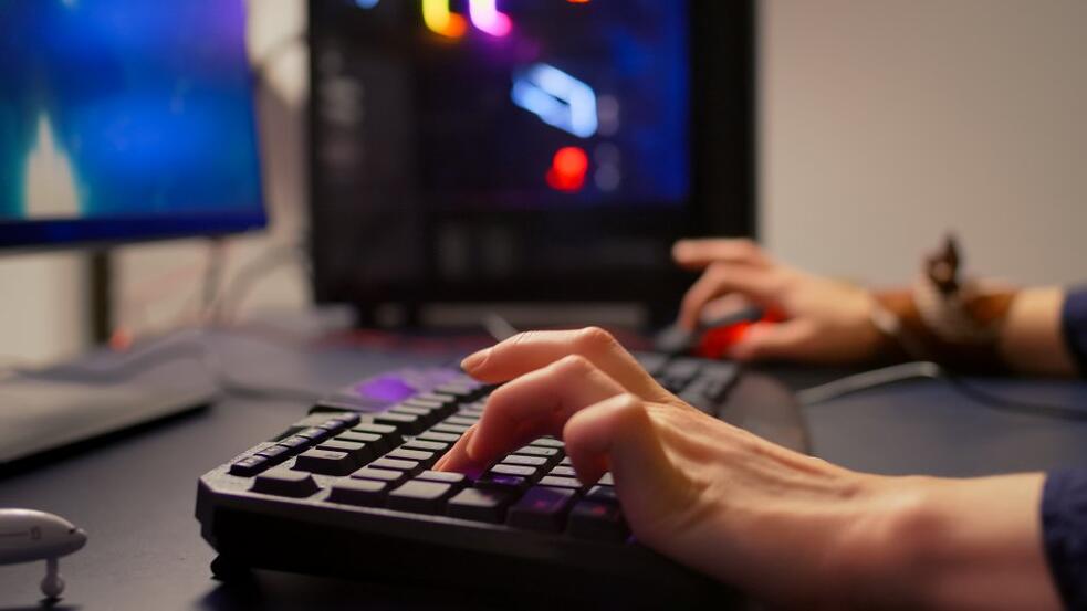 Handen typen op een toetsenbord met computerscherm op de achtergrond.