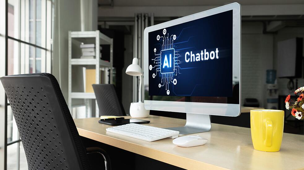 Kantoor met computer die "AI Chatbot" toont, naast gele mok en lamp.