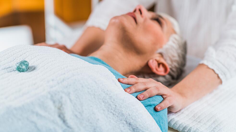 Persoon ondergaat ontspanningsbehandeling met hand op schouder.